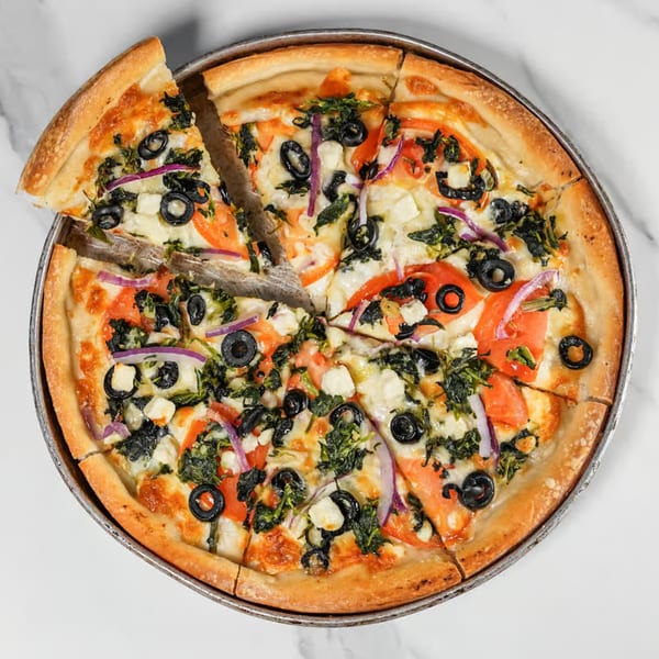 A sliced 5 Herb Pizza with tomatoes, black olives, spinach, red onions, and feta cheese.