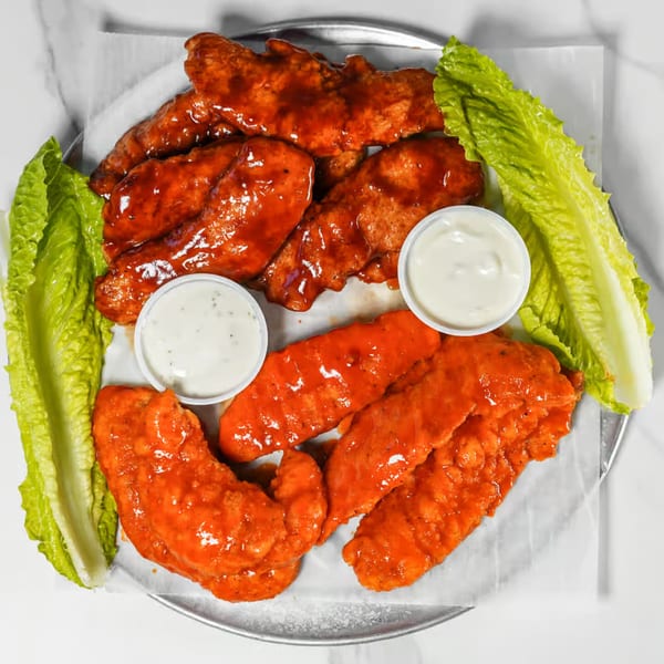 Two rows of chicken tenders, one BBQ and one buffalo, with ranch and lettuce on a metal tray.