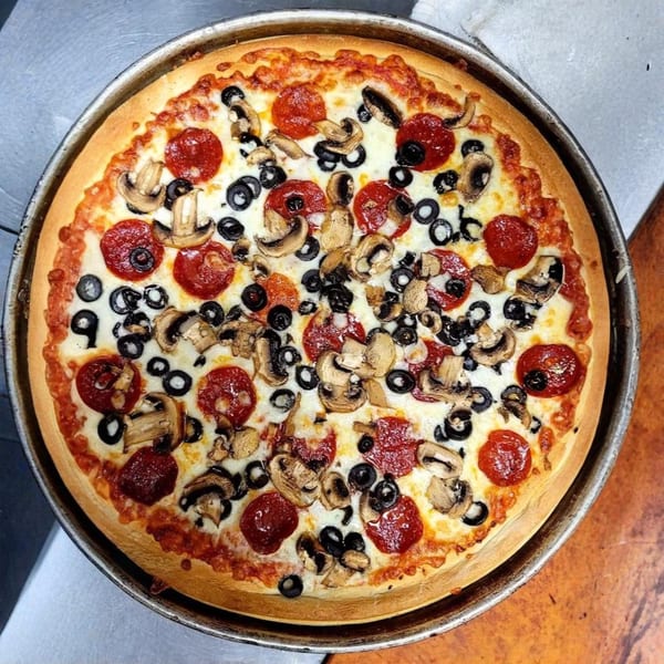 A 5 Herb Pizza with pepperoni, mushrooms, and black olives in a metal pan.