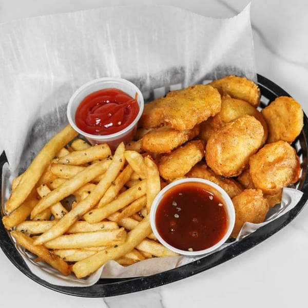 A basket of golden-brown chicken nuggets and french fries with ketchup and sweet and sour sauce.